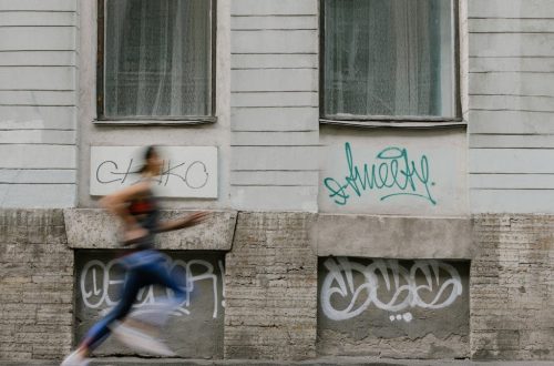 Blurred motion of a woman running past a graffiti-covered urban wall. Captures dynamic energy.